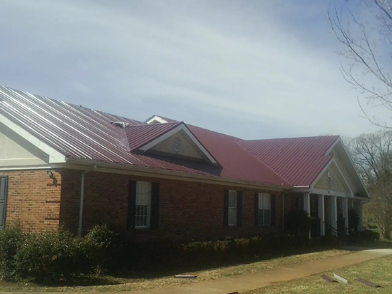 Red metal roof with gabled entries on a long brick building, from a Hail Damage Roof Repair job in Hall