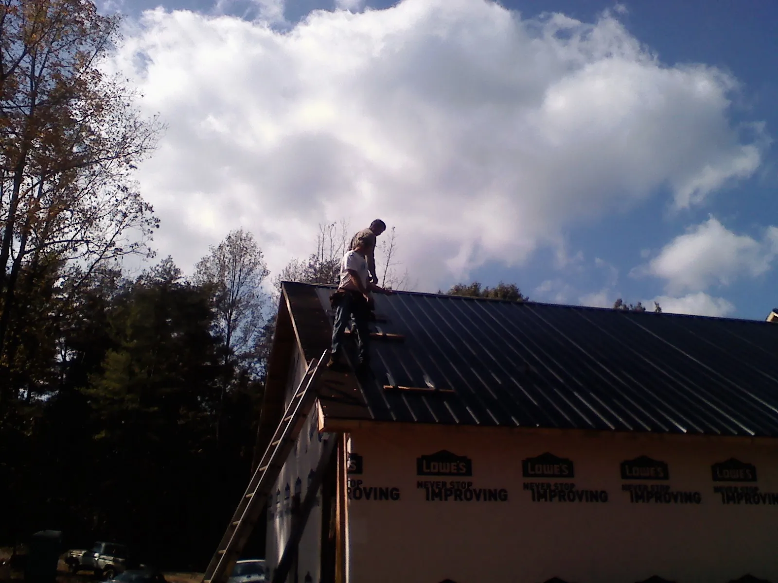 Roofer fastening dark metal panels high against a cloudy sky, from a Roof Inspection job in Hall