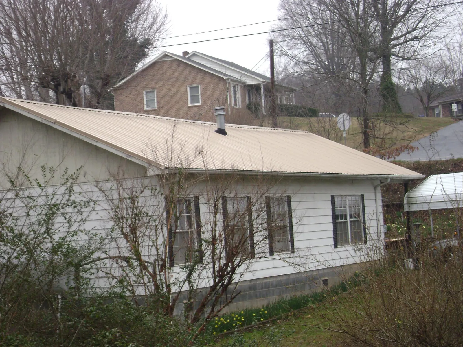 Tan metal roof on a white sided house set into a hillside — Commercial Roofing by Roofing Brothers in Hall