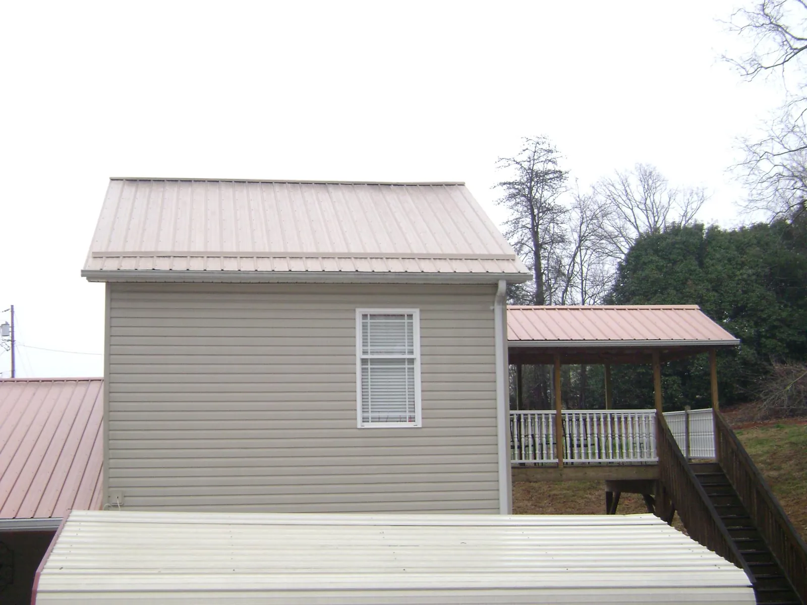 Tan metal roofs on a two story addition and attached porch, from a Roof Replacement job in Hall